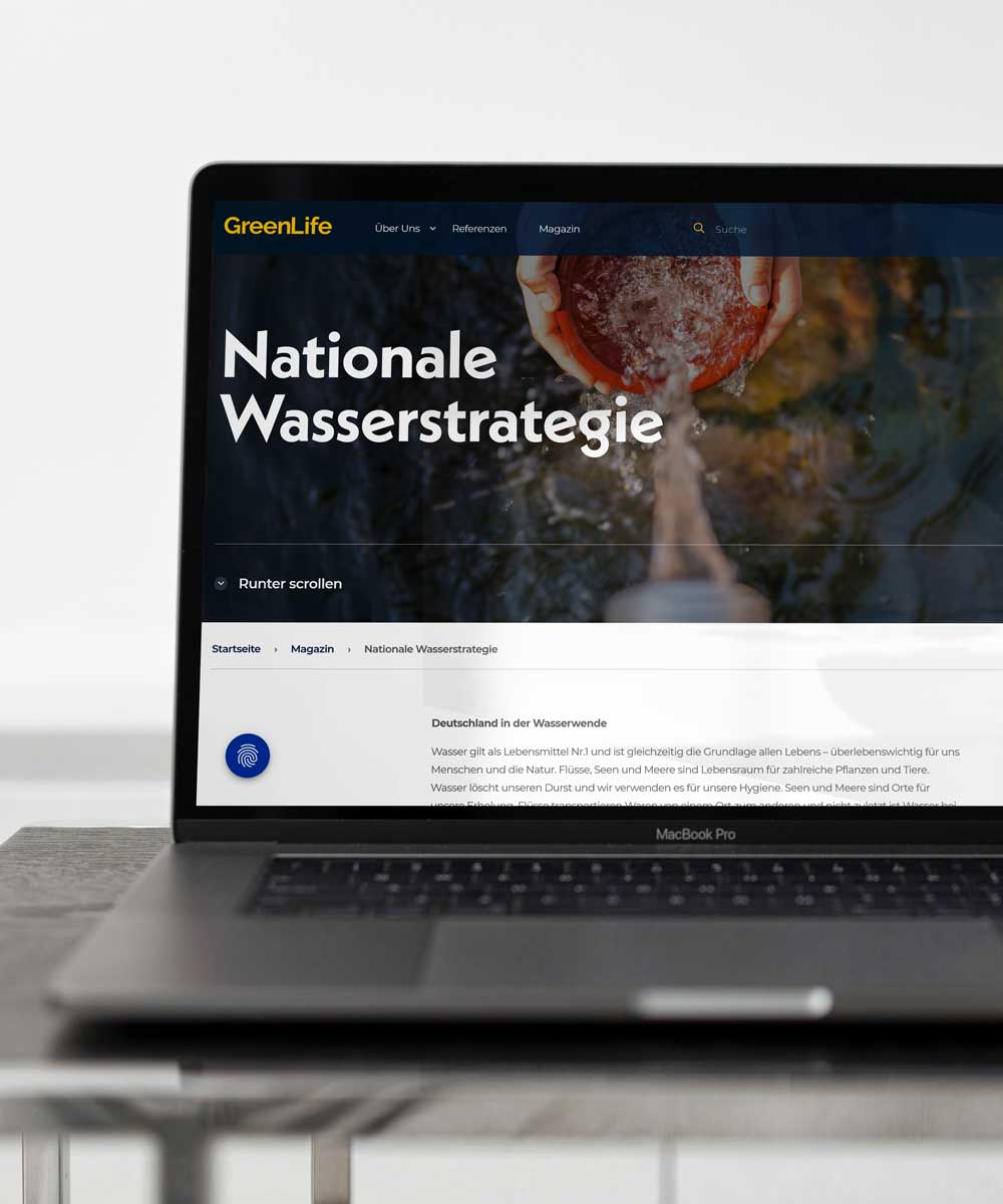 Ein geöffneter Laptop zeigt die Website „GreenLife“ mit dem Webseiten-Titel „Nationale Wasserstrategie“ und einem Hintergrundbild von Händen, die Wasser aus einem fließenden Strom schöpfen. Darunter befindet sich eine Textüberschrift über Deutschland und die Wasserwende.
